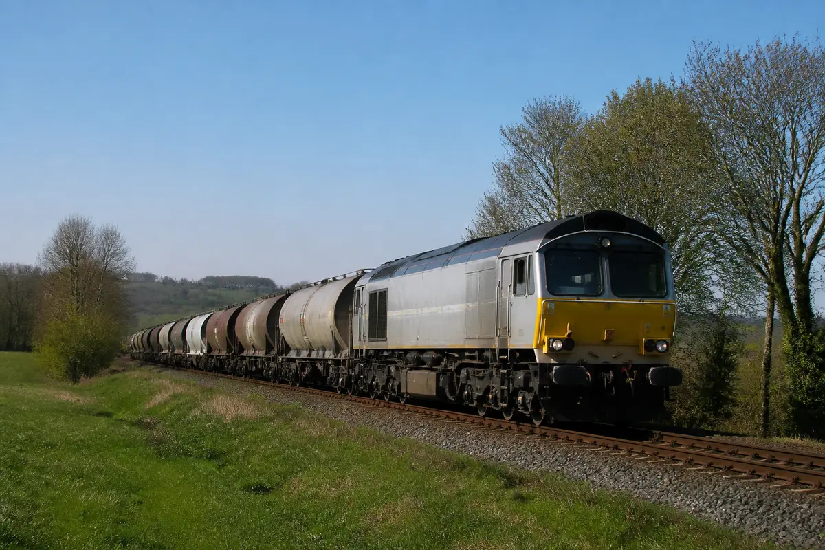 Train de fret VFLI traversant une campagne verdoyante avec des wagons-citernes en arrière-plan