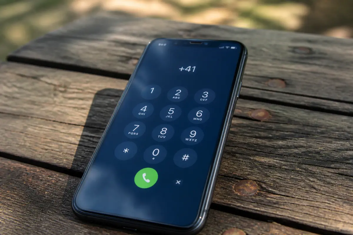 Téléphone affichant indicatif 41 sur écran de numérotation posé sur table en bois