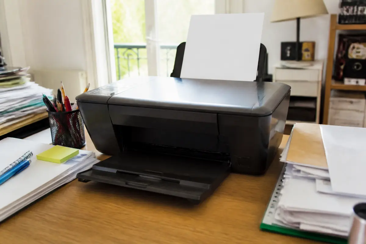 Imprimante sur un bureau avec feuilles, un livre ouvert et autres objets en arrière-plan