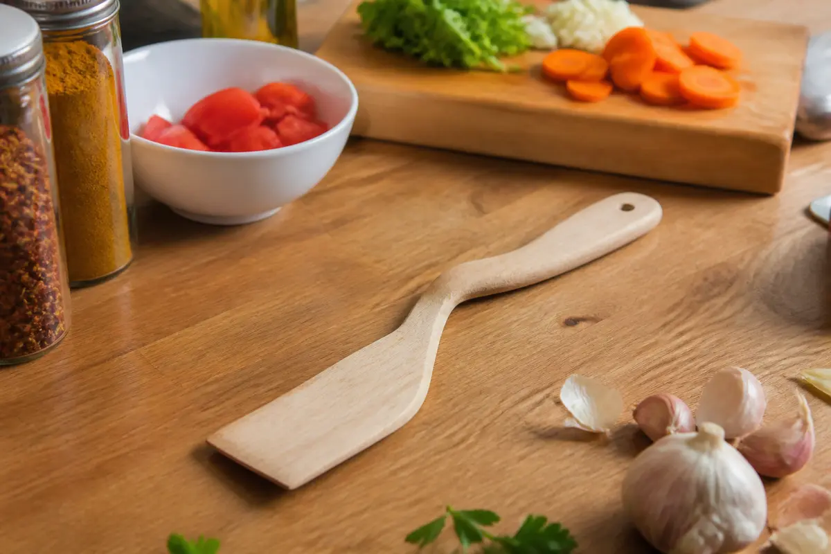 Spatule en bois, légumes frais et épices sur planche de cuisine avec objet en bois.
