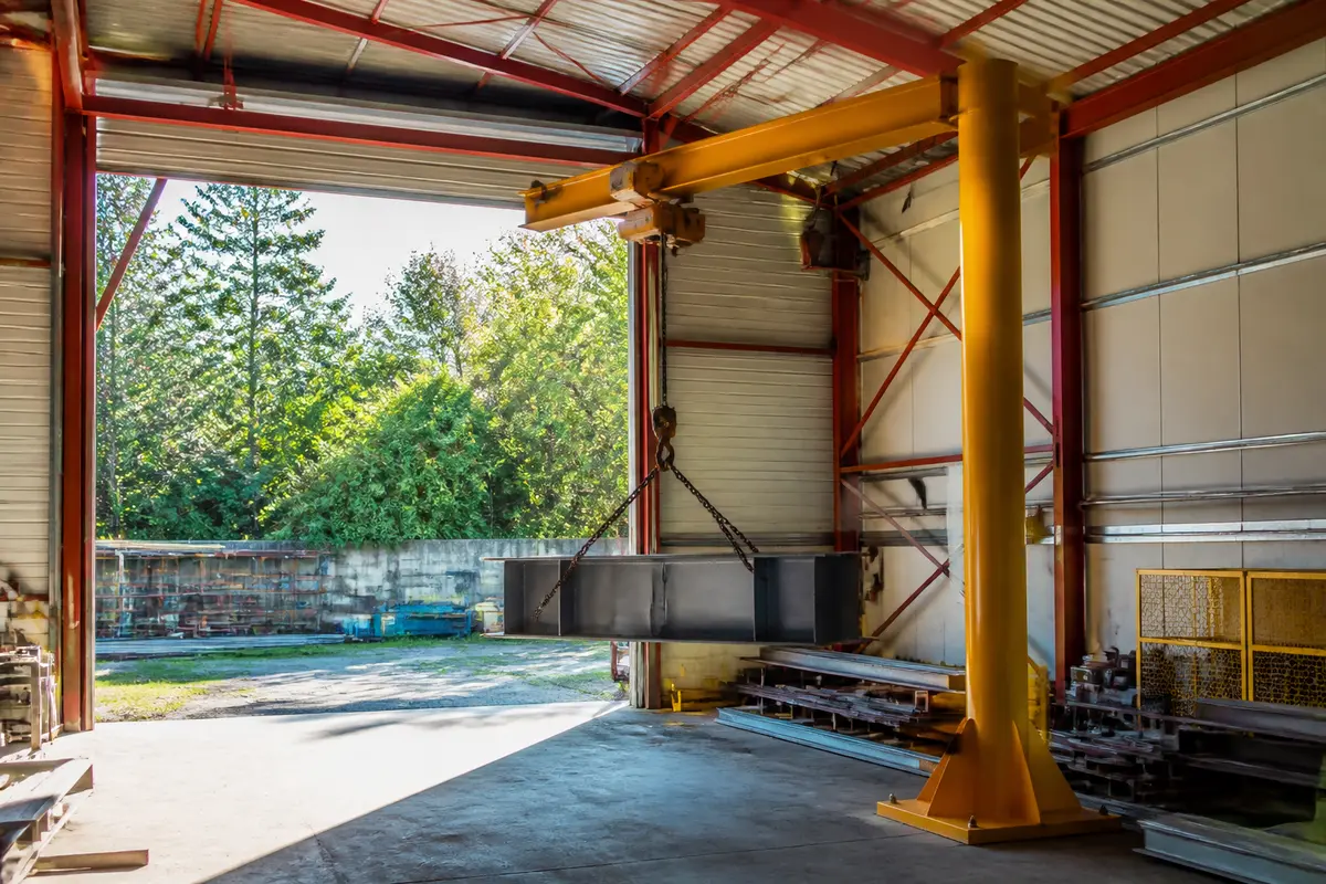 Grue industrielle manipulant une lourde poutre métallique pour le levage et manutention en entrepôt