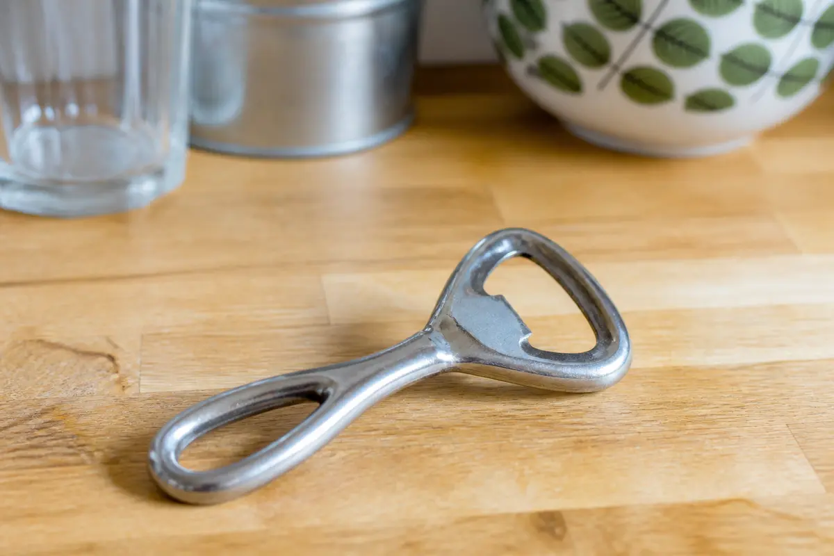 Ouvre-bouteille en métal posé sur une table de cuisine en bois.