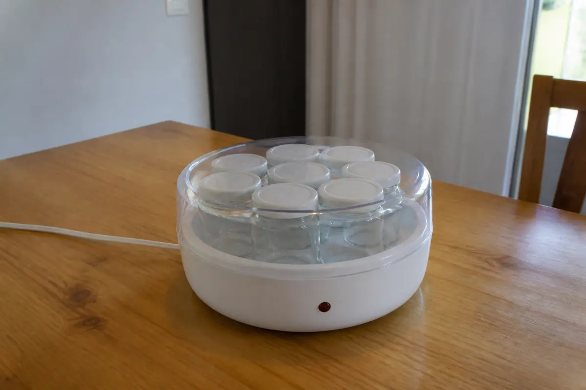 Yaourtière blanche avec pots sur table en bois, un objet en plastique transparent