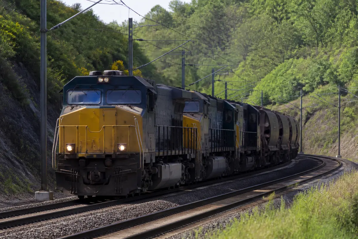 Train de fret traversant un paysage verdoyant sur des rails électrifiés en pleine journée